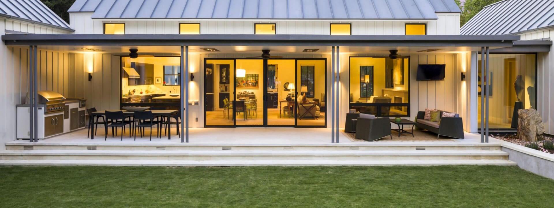 Covered patio with black-framed windows and wide glass doors opening onto a lawn